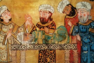 A historic illustration depicting an operation with medieval Islamic physicians. One patient lies on a table while three doctors dressed in traditional robes and turbans tend to him, one holding his wrist and the others examining and discussing the patient.