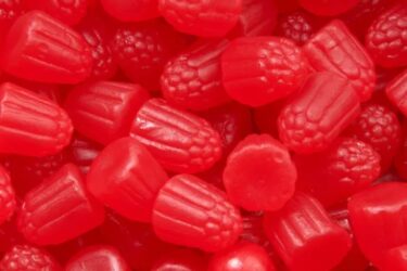 Close-up of assorted red gummy candies with various textures and shapes, resembling berries and fruit.