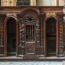 A traditional wooden confessional booth with ornate carvings and two entry arches, located in an ornate church setting. The central section is intricately detailed, featuring decorative columns and woodwork.