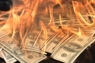 A stack of hundred-dollar bills is engulfed in bright orange flames, creating a dramatic and intense scene symbolizing financial loss or waste.