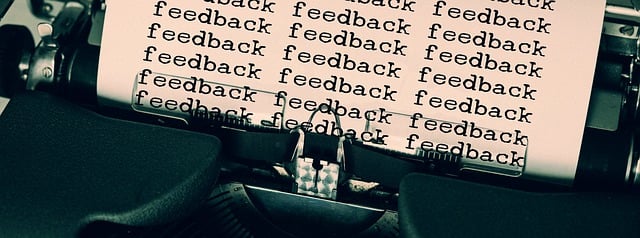 Close-up of a typewriter with the word "feedback" repeatedly typed on a sheet of paper, filling the entire visible area. The typewriter keys and mechanism are partially visible.