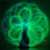 A person stands in the center of intricate, neon-green light trails forming a circular, flower-like pattern against a dark background. The light trails create a sense of movement and energy around the person.