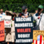 A group of protesters holding signs at a rally. Signs say "Vaccine Mandates Violate Bodily Autonomy," "My Body My Choice," "I am informed I do not consent," and other slogans. Some wear hats and carry flowers.