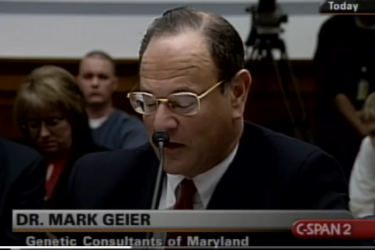 A man wearing glasses and a suit, identified as Dr. Mark Geier, speaks into a microphone at a hearing. The C-SPAN2 logo appears on-screen, with “Geier” and “Genetic Consultants of Maryland” displayed. Several people sit in the background.