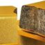 Several gold bars are stacked, but one bar is cut open to reveal a gray, rough interior, indicating that it is not solid gold.