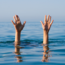 Two hands are raised above the surface of a body of water, suggesting a person is struggling or in distress, possibly drowning, with a clear blue sky and calm water in the background.