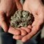 A person holding a large, shiny, metallic-looking rock with both hands. The rock appears rough and glittery, resembling a lump of pyrite or "fool's gold.