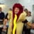 A man in a hot dog costume gestures animatedly while standing in front of a group of people in an office setting, some of whom appear amused or bemused.