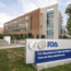 A modern brick and glass building with a sign in front reading "U.S. Department of Health and Human Services, Food and Drug Administration (FDA)" on a landscaped campus.