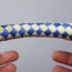 Two hands with index fingers inserted into a blue and beige woven Chinese finger trap against a plain background.
