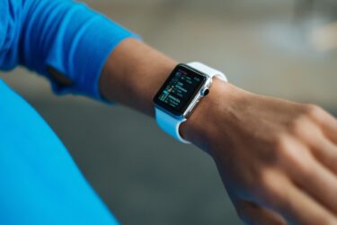 A person wearing a blue long-sleeve shirt checks a white smartwatch on their wrist, displaying a colorful screen with time and fitness activity data.