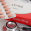 A close-up of a box labeled "Statin Tablets 40 mg" with a blister pack of round pink tablets, a stethoscope, and part of a prescription pad in the background.
