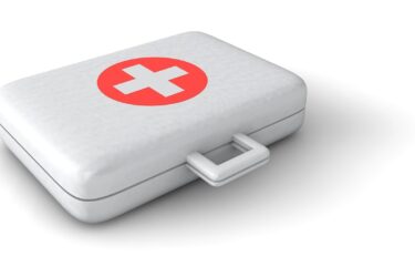 A white first aid kit box with a red circle and a white cross on the lid, placed on a white surface.