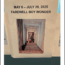 A printed sign reads "May 6 – July 29, 2025 Farewell Boy Wonder" above a photo of a person with luggage walking down a hallway. The sign is taped to a surface.