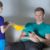 A boy hands a stack of papers to a serious-looking man sitting on a couch, who holds a TV remote and looks away from the boy.