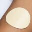 A close-up of a person's upper arm wearing a white sleeveless shirt, with a large beige adhesive patch applied to their skin.