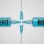 Two syringes filled with blue liquid face each other, labeled "BENEFIT" on the left and "RISK" on the right, with their needles nearly touching in the center.
