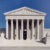 The front view of the United States Supreme Court building in Washington, D.C., featuring tall columns, statues, steps leading to the entrance, and a clear blue sky overhead.