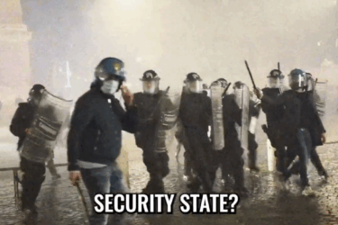 A group of riot police in helmets and shields stand in a foggy, wet street at night. One officer faces the camera. Text at the bottom reads, "SECURITY STATE?.