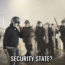 A group of riot police in helmets and shields stand in a foggy, wet street at night. One officer faces the camera. Text at the bottom reads, "SECURITY STATE?.