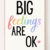 A framed sign with the words "BIG feelings ARE OK" in bold black and pastel rainbow letters, with a pink heart next to "OK" on a white background.