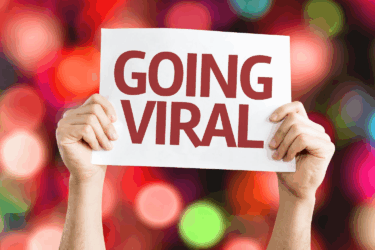 A person holds up a white sign with bold red text reading "GOING VIRAL" against a colorful, blurred background of bokeh lights.