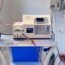A medical machine processes blood through tubes attached to a patient’s arm, which is resting on a table; the setup is in a clinical room with various medical devices.