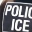 A close-up of the back of a person wearing a vest labeled "POLICE ICE," indicating they are part of the U.S. Immigration and Customs Enforcement agency. The background is blurred.