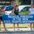 Four people stand on a sidewalk holding a large blue banner that reads, "Medical Freedom Is The New Civil Rights Movement." Two women wear shirts with protest slogans. Cars are parked in the background.