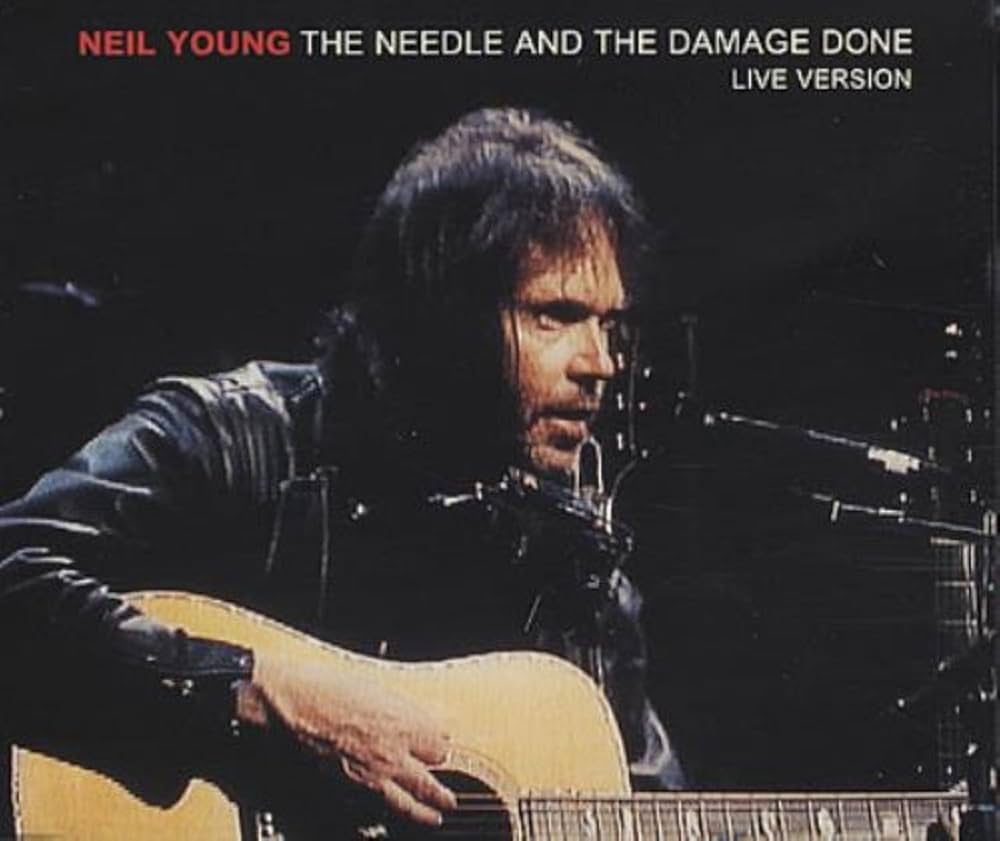 A man in a leather jacket plays an acoustic guitar and sings into a microphone on stage. The text reads, "NEIL YOUNG THE NEEDLE AND THE DAMAGE DONE LIVE VERSION.