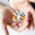 A pair of hands holds a variety of colorful pills and capsules, including white, blue, orange, and pink medications, against a light background.