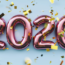 Shiny pink balloon numbers forming "2020" with gold confetti falling in front of a light blue background, creating a festive atmosphere.