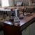 A laboratory with wooden workbenches, equipment, open drawers, bottles, and a labeled flask of clear liquid on the counter. The room appears well-lit with windows in the background.