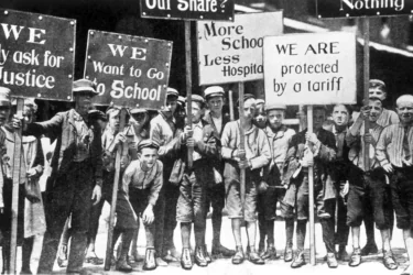 A group of boys holding protest signs advocating for justice and education, with messages like "We Want to Go to School" and "More School Less Hospital." The image appears to be from the early 20th century.