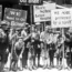 A group of boys holding protest signs advocating for justice and education, with messages like "We Want to Go to School" and "More School Less Hospital." The image appears to be from the early 20th century.
