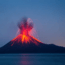 A volcano erupts at night, spewing bright orange lava and ash into the dark blue sky, with molten streams flowing down its slopes and a calm body of water in the foreground.