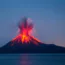 A volcano erupts at night, spewing bright orange lava and ash into the dark blue sky, with molten streams flowing down its slopes and a calm body of water in the foreground.