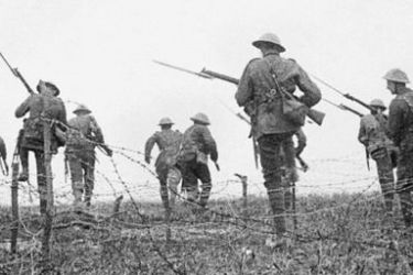 World War I soldiers wearing helmets and carrying rifles advance through a barbed wire field, moving forward in formation on a battlefield.