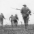 World War I soldiers wearing helmets and carrying rifles advance through a barbed wire field, moving forward in formation on a battlefield.