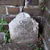 A weathered, white marble tombstone sits against a cracked brick wall. The inscription reads: “Our Baby” followed by “DIED DEC. 3, 1845.” Small green weeds and leaves grow in the dirt around the base of the headstone.