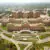 Aerial view of a large, multi-winged brick hospital complex surrounded by parking lots and wooded grounds.