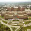 Aerial view of a large, multi-winged brick hospital complex surrounded by parking lots and wooded grounds.